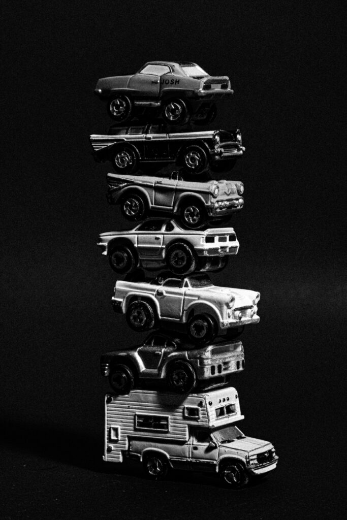 Black and white image of stacked toy cars on a black background.