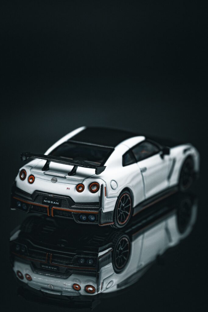 White Nissan GT-R RC car on reflective dark surface, showcasing sleek design and detailing.