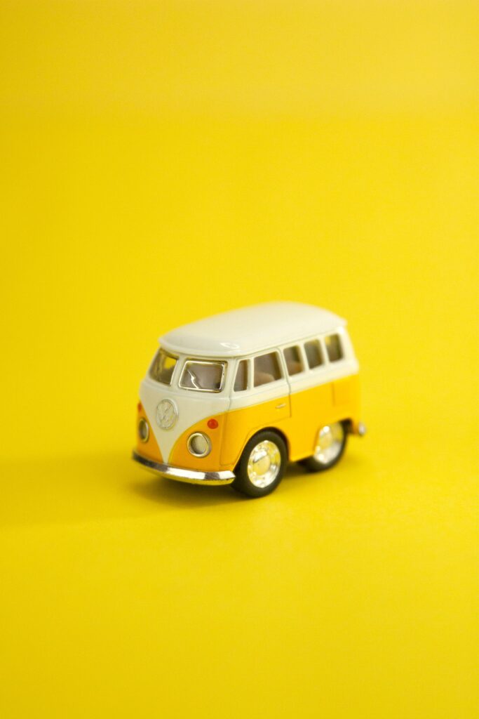 Miniature toy and analogue of yellow and white vintage camping trailer placed on centre of bright yellow background